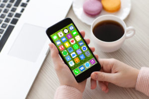 woman hands holding white phone with home screen icons apps near notebook